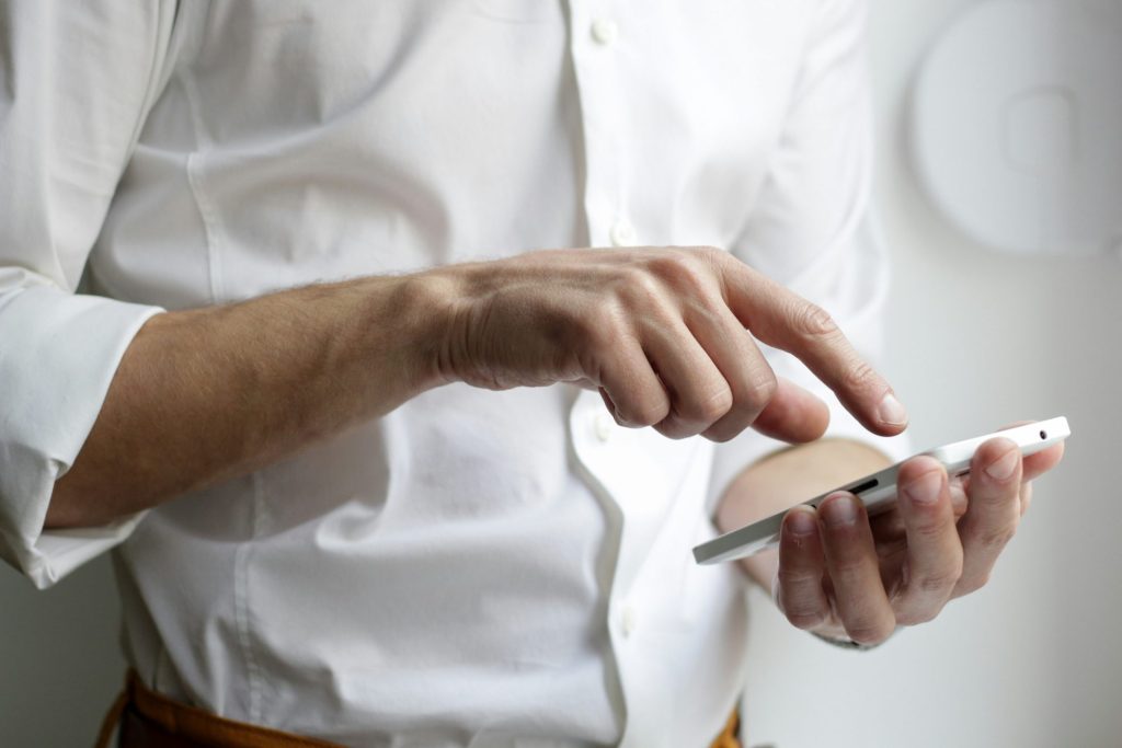 Herr in weissem Hemd mit Smartphone in der Hand